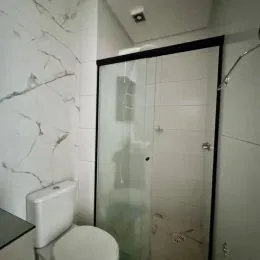 Banheiro com paredes de mármore branco e box de vidro transparente.