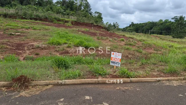 Vista de um terreno gramado com vegetação e uma placa no meio.