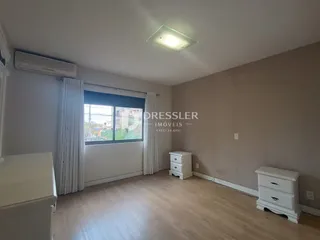 Quarto com piso de madeira e cortinas brancas.