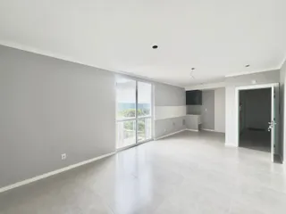 Sala de estar ampla com piso claro e grandes janelas de vidro.