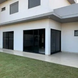Fachada de uma residência branca com grandes portas de vidro e gramado em primeiro plano.
