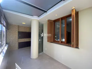 Ambiente interno de uma sala de estar com piso de cerâmica e grandes janelas de madeira.