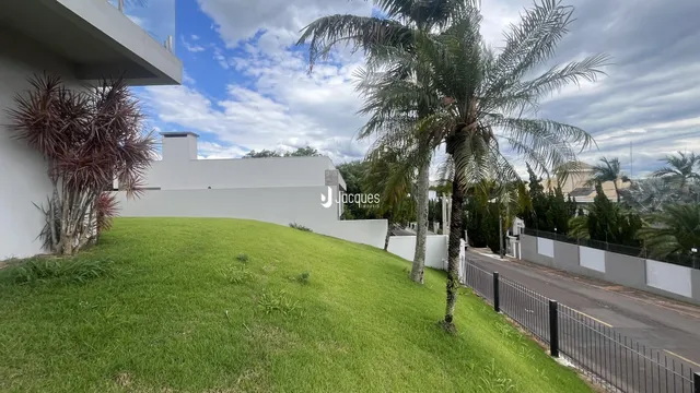 Fachada de uma residência com gramado e palmeiras ao lado de uma estrada.