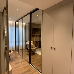 Vista interna de um corredor com piso de madeira e parede espelhada.