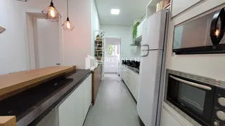 Vista interna de uma cozinha moderna com armários brancos e bancadas escuras.