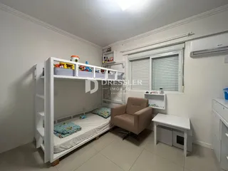 Quarto com cama de beliche e poltrona em ambiente claro.