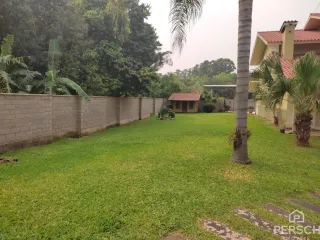 Gramado verde bem cuidado com cerca e vegetação ao fundo.