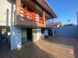 Fachada de uma residência com varanda e área externa pavimentada.