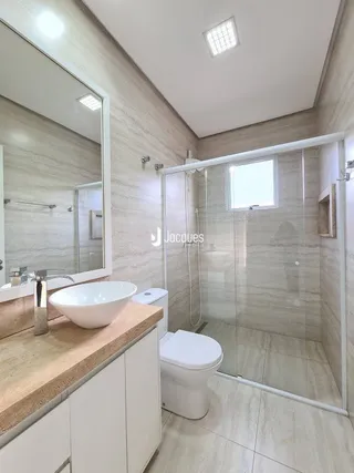 Banheiro com box de vidro e revestimento claro.
