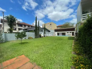 Vista externa de um quintal gramado com cerca e piscina ao fundo.