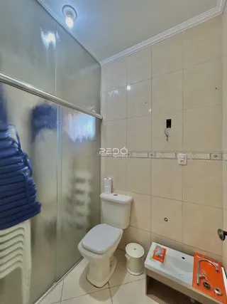 Foto interna de um banheiro com revestimento cerâmico e box de vidro.