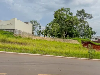Vista externa de uma propriedade com terreno gramado e vegetação ao fundo.