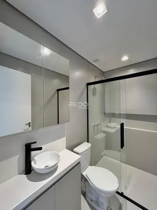 Banheiro moderno com box de vidro e louças brancas.