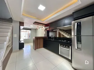 Ambiente moderno de sala e cozinha com piso claro e armários escuros.