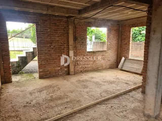 Vista interna de uma estrutura com paredes de tijolo aparente e piso de terra.