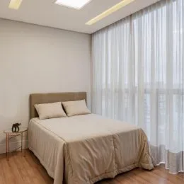 Quarto com cama de casal e cortinas claras.