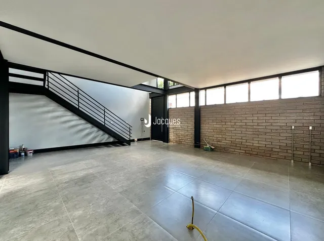 Vista interna de um espaço amplo com escadaria e parede de tijolos exposta.