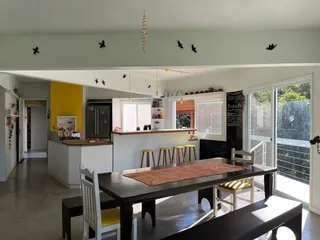 Ambiente de sala de jantar e cozinha com mesa de madeira escura e acesso a uma área externa.