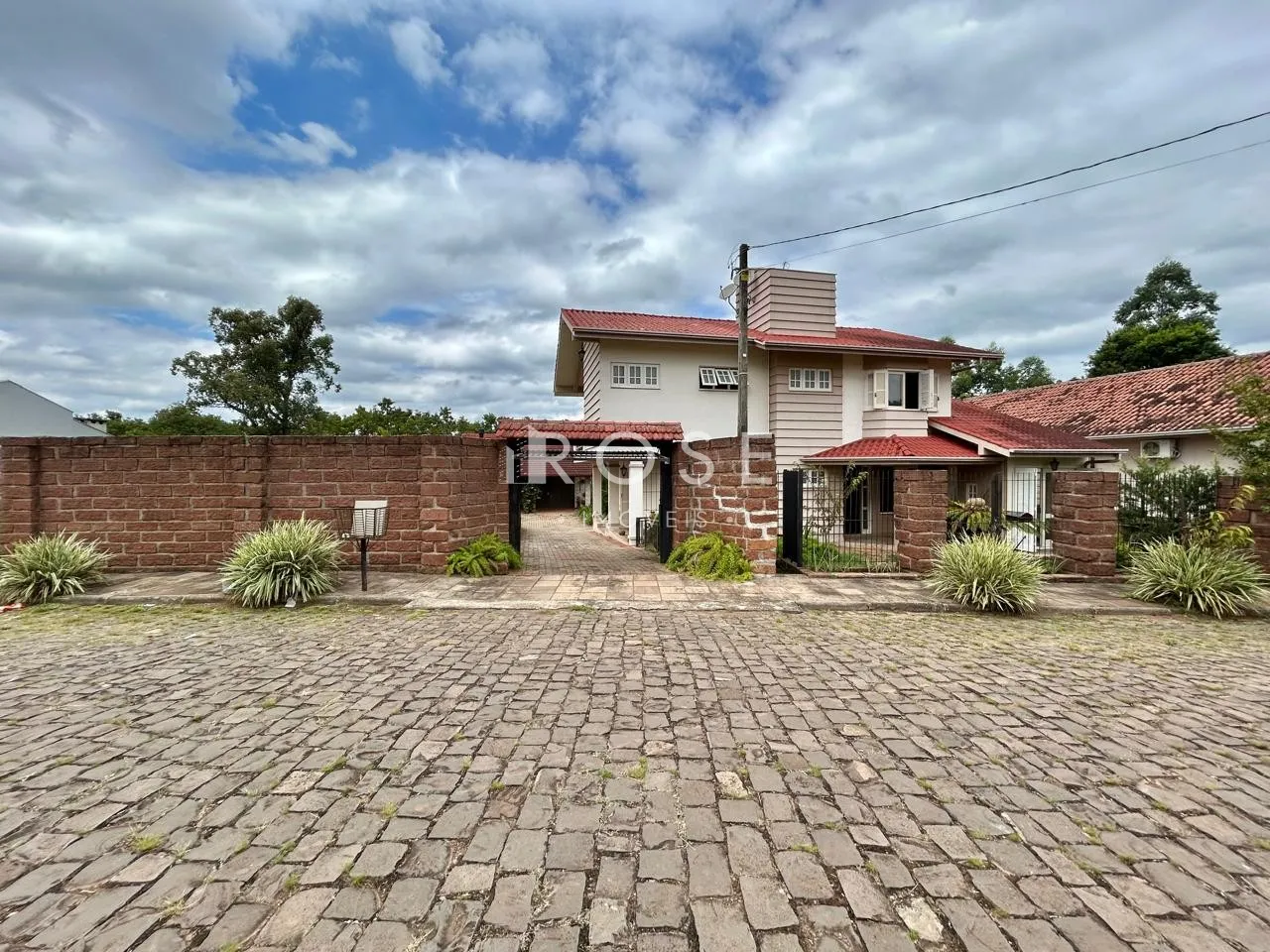 Fachada de uma casa com muro de tijolos e pátio pavimentado em Lajeado, Brasil.