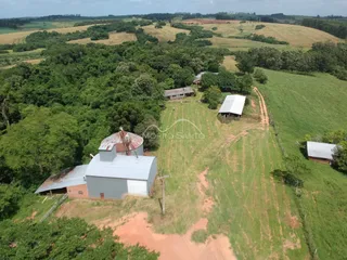Vista aérea de uma propriedade rural com construções rústicas em meio a campos e mata.