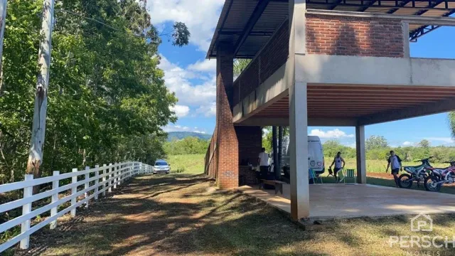Vista externa de uma propriedade com cerca branca e vegetação ao fundo.