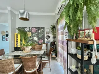 Ambiente interno de uma sala de jantar com móveis de vime e decoração floral.