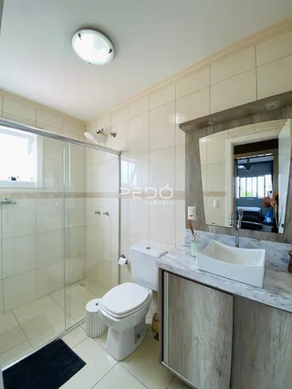 Banheiro com revestimento cerâmico e box de vidro.