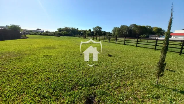 Campo verde com cerca de madeira e vegetação ao fundo.