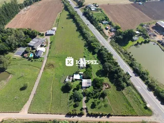 Vista aérea da propriedade mostrando campos abertos e estruturas rurais ao longo de uma estrada.