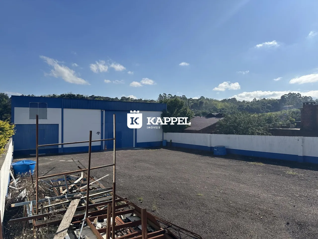 Foto da fachada de um galpão industrial azul com área de terreno em frente.