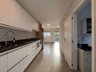 Cozinha com armários brancos e bancadas escuras em um corredor de casa.