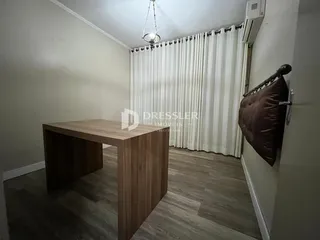 Ambiente interno de uma sala com piso de madeira e cortinas brancas.