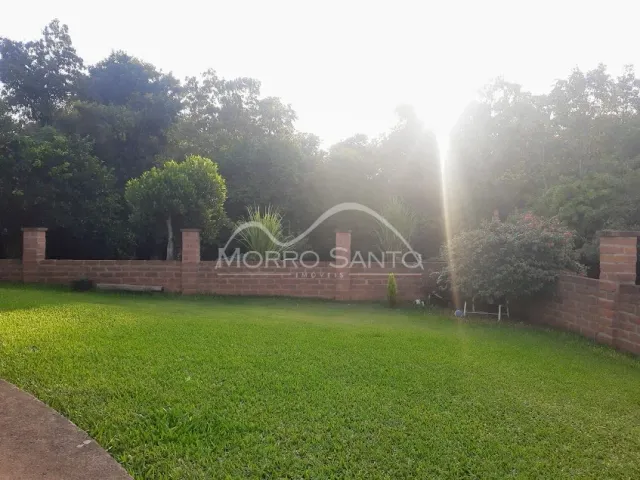 Foto externa mostrando um gramado verde com um muro de tijolos e vegetação ao fundo.