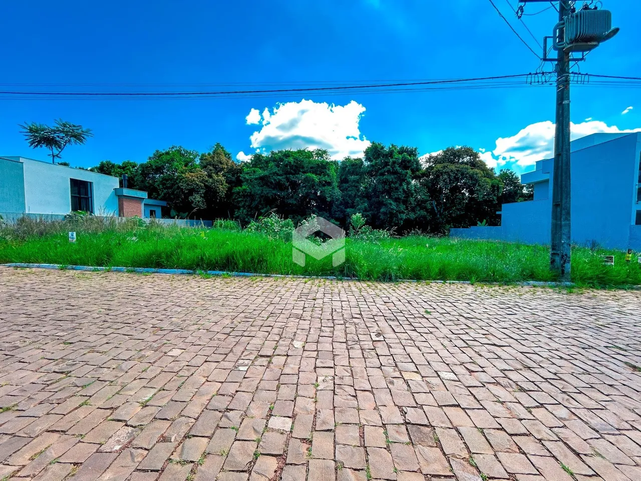 Vista externa de uma propriedade com área pavimentada e vegetação ao fundo.