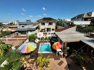 Foto da área externa com piscina e espreguiçadeiras em um jardim.