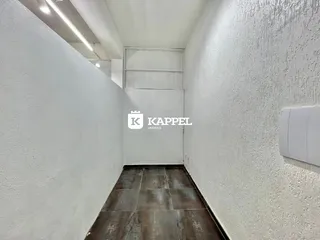 Foto de um corredor interno com paredes brancas e piso de ladrilho escuro.