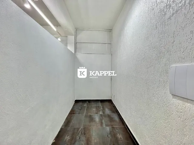 Foto de um corredor interno com paredes brancas e piso de ladrilho escuro.