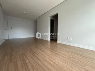Ambiente interno de uma sala com piso de madeira clara e paredes brancas.