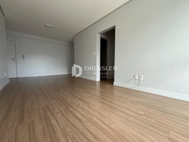 Ambiente interno de uma sala com piso de madeira clara e paredes brancas.