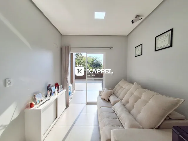 Sala de estar com sofá claro e paredes brancas, com porta de vidro que dá acesso ao exterior.