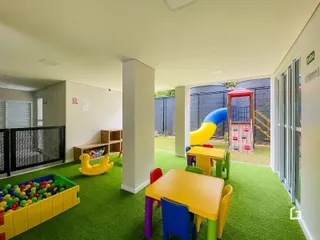 Ambiente interno com piso verde e brinquedos coloridos em uma área de lazer.