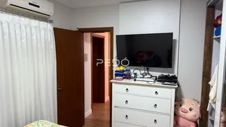 A sala de estar possui uma parede com televisão e uma janela coberta por cortinas brancas.