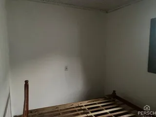 Vista interna de um cômodo com paredes brancas e piso de madeira aparente.