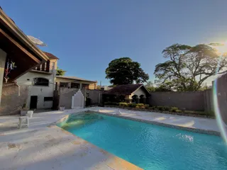 Uma foto externa mostra uma piscina com área pavimentada em uma propriedade.