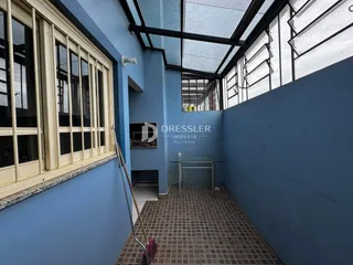 Corredor com grandes janelas e piso de cerâmica em uma residência.