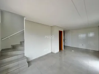 Vista interna de uma sala de estar com escadaria e paredes brancas.