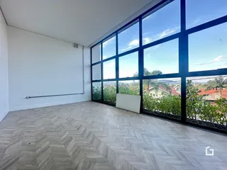 Sala de estar com piso de madeira e grandes janelas que dão vista para a paisagem.