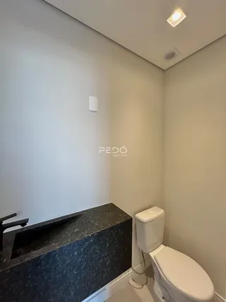 Foto interna de um banheiro com bancada escura e vaso sanitário branco.