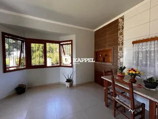 Uma foto interna mostra uma sala com grandes janelas e uma mesa de jantar de madeira.