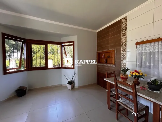 Uma foto interna mostra uma sala com grandes janelas e uma mesa de jantar de madeira.